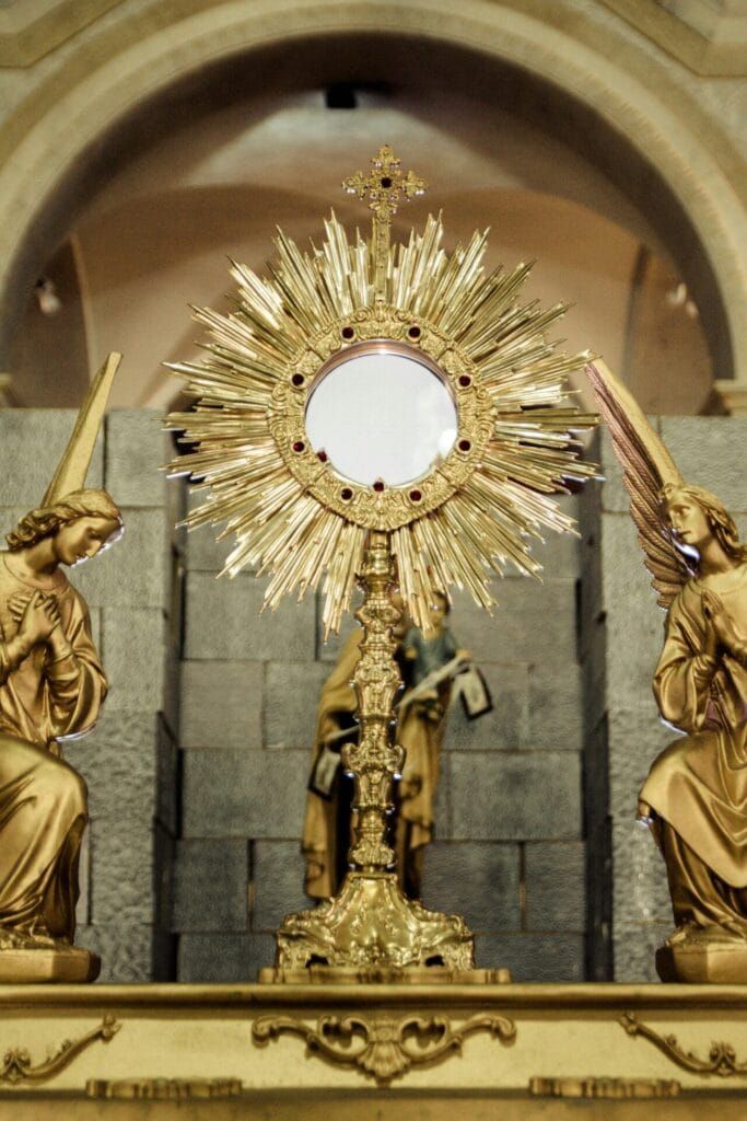 Golden monstrance flanked by angel statues in a church setting, emphasizing spirituality and religion.